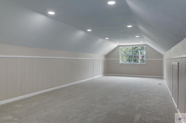 additional living space featuring light colored carpet, lofted ceiling, and wooden walls