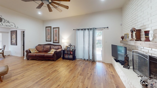 living room with ceiling fan, a brick fireplace, and light hardwood / wood-style flooring