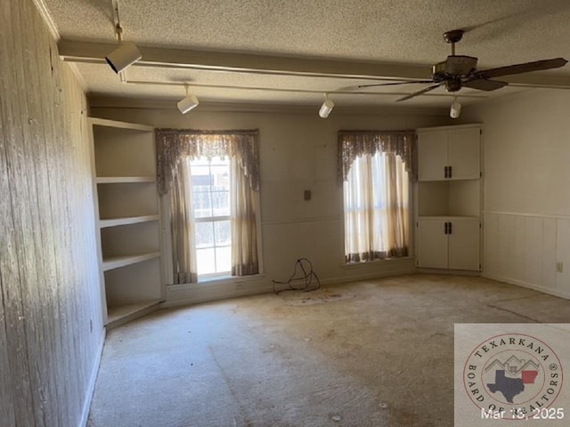 unfurnished room with a ceiling fan, a wainscoted wall, carpet floors, and a textured ceiling