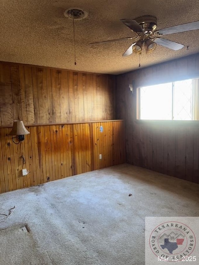 carpeted spare room with visible vents, wooden walls, a textured ceiling, and a ceiling fan