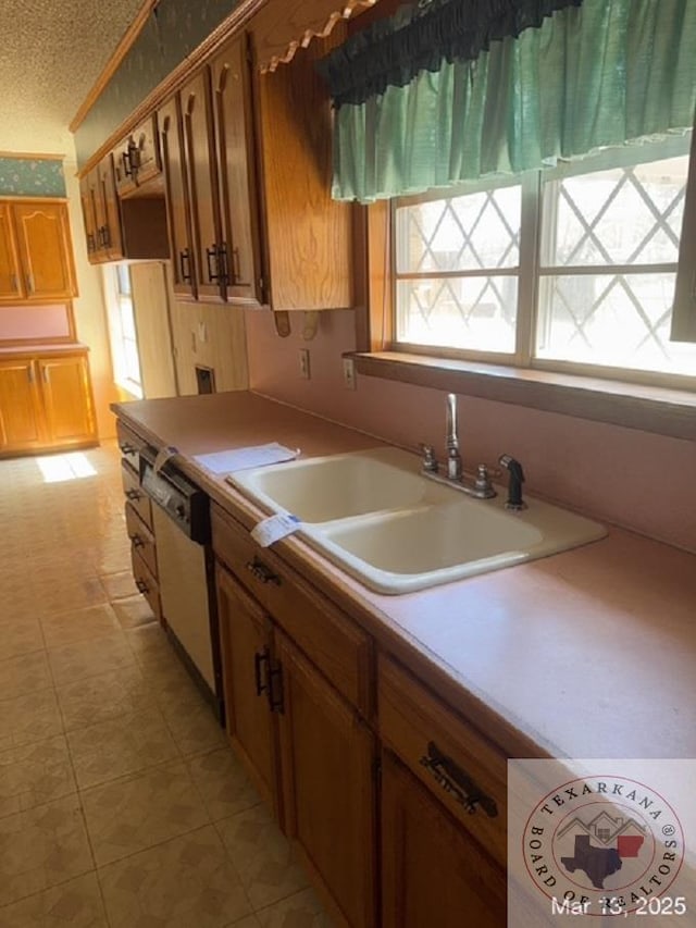 kitchen featuring a textured ceiling, white dishwasher, light countertops, and a sink