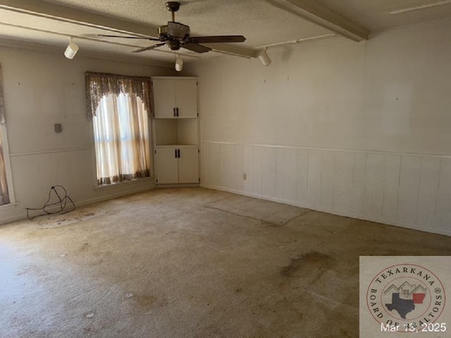 spare room with a wainscoted wall, beamed ceiling, a textured ceiling, carpet, and ceiling fan