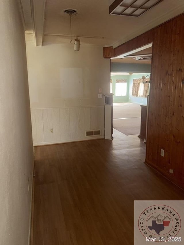 corridor with visible vents, beamed ceiling, wood walls, wainscoting, and wood finished floors