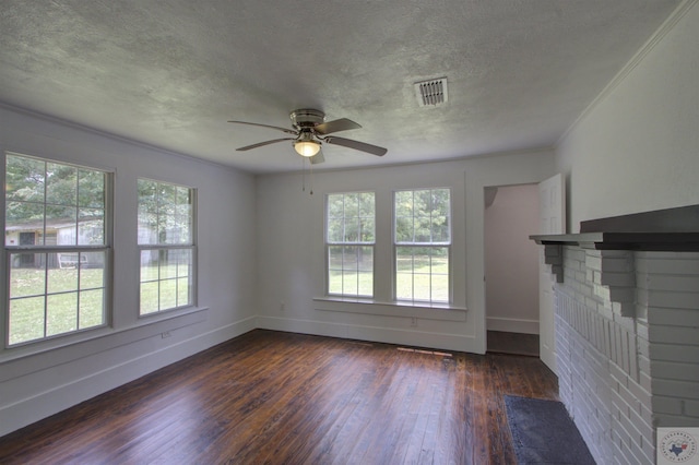 unfurnished living room featuring ceiling fan, dark hardwood / wood-style flooring, a brick fireplace, a textured ceiling, and ornamental molding