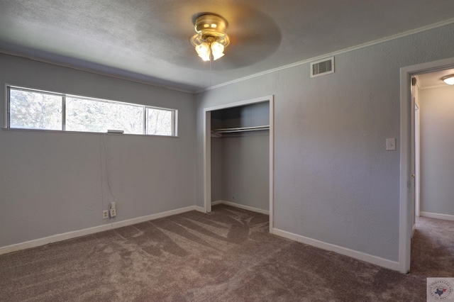 unfurnished bedroom with a closet, ceiling fan, dark colored carpet, and crown molding