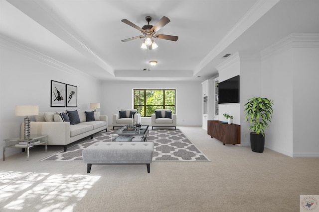 living room with ceiling fan, ornamental molding, light carpet, and a tray ceiling