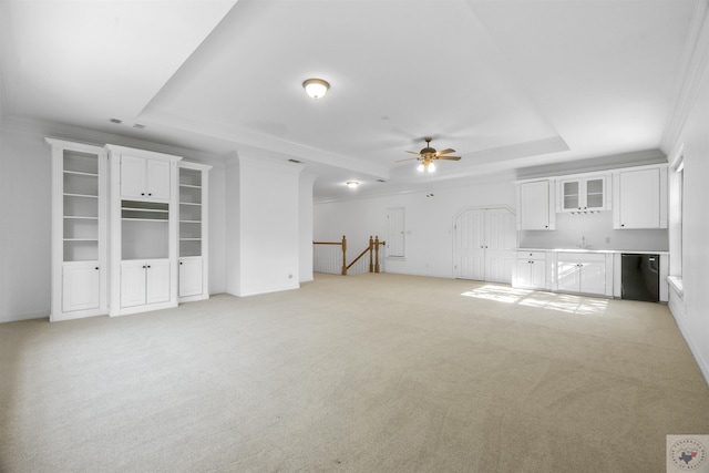 unfurnished living room featuring ceiling fan, light colored carpet, a tray ceiling, indoor wet bar, and ornamental molding