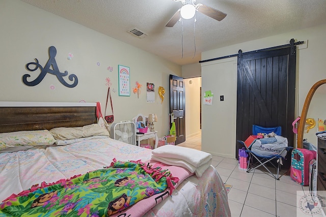 tiled bedroom featuring a textured ceiling, ceiling fan, and a barn door