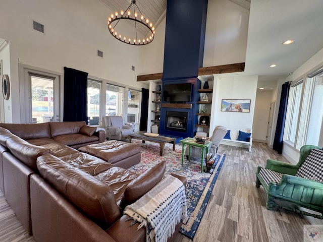 living room featuring visible vents, light wood-style flooring, a large fireplace, and an inviting chandelier