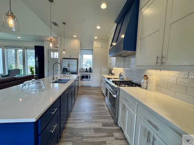 kitchen featuring visible vents, a sink, stainless steel appliances, blue cabinets, and wall chimney exhaust hood