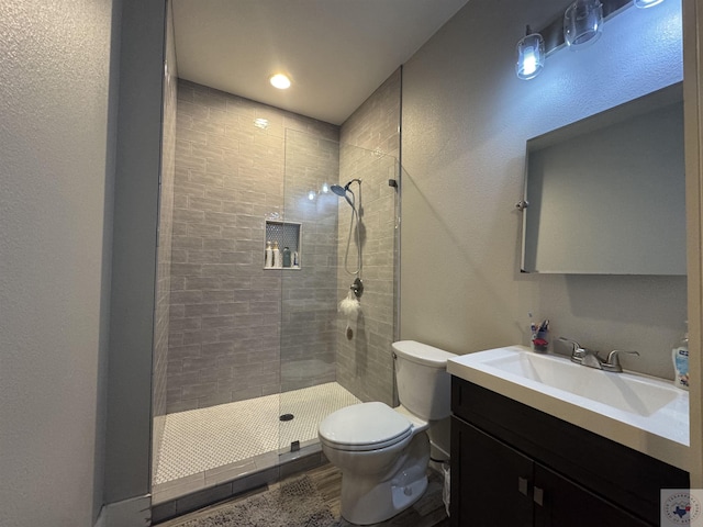 full bathroom featuring a tile shower, toilet, and vanity