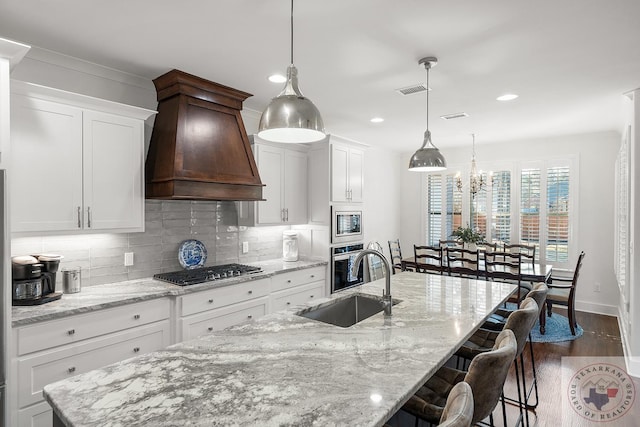 kitchen featuring a breakfast bar, custom exhaust hood, stainless steel appliances, backsplash, and a sink