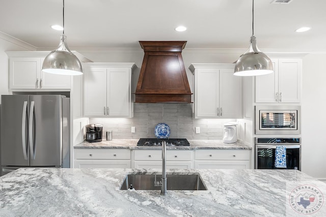 kitchen featuring tasteful backsplash, white cabinets, custom range hood, appliances with stainless steel finishes, and a sink