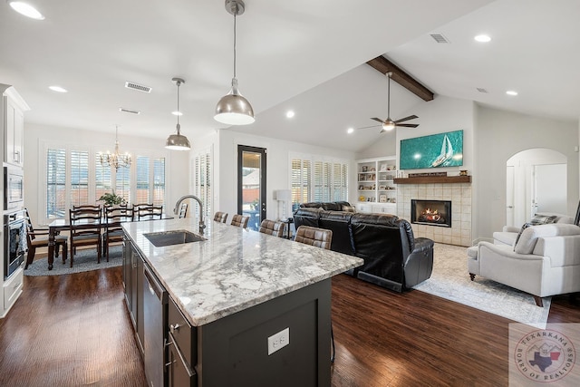 kitchen with dark wood finished floors, vaulted ceiling with beams, a fireplace, stainless steel appliances, and a sink