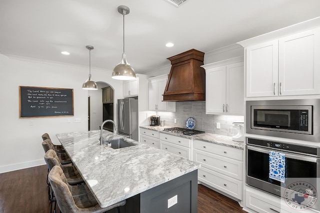 kitchen featuring dark wood-style floors, custom exhaust hood, decorative backsplash, appliances with stainless steel finishes, and a kitchen island with sink