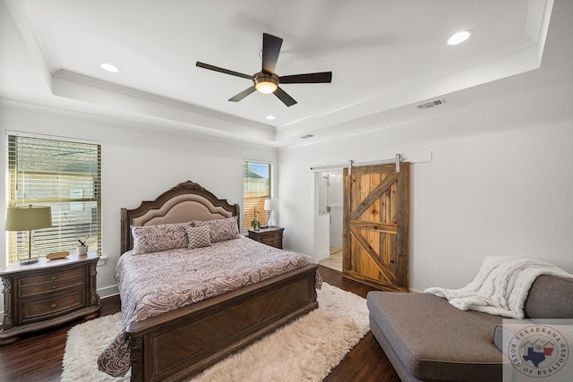 bedroom with dark wood finished floors, a barn door, a raised ceiling, and visible vents