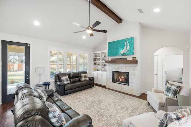 living room with arched walkways, visible vents, wood finished floors, a tile fireplace, and beamed ceiling