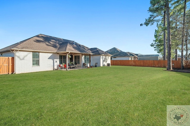 rear view of house with a yard, brick siding, and a fenced backyard