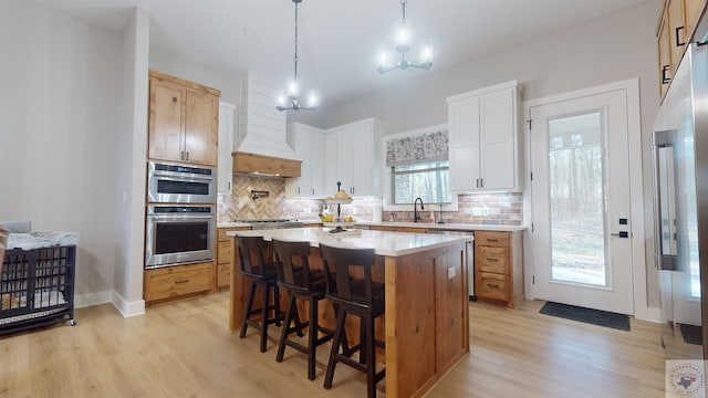 kitchen with appliances with stainless steel finishes, white cabinetry, decorative backsplash, a kitchen island, and decorative light fixtures