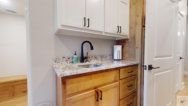 bar featuring light stone counters, sink, and white cabinets