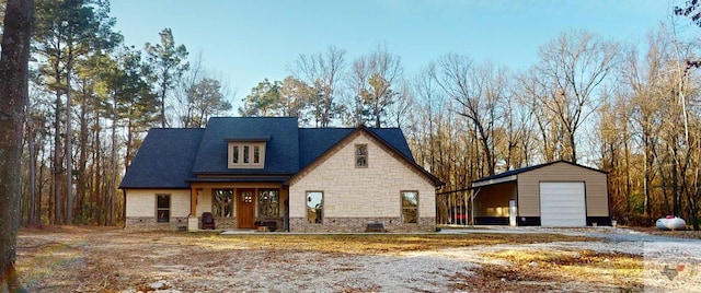 view of front of property featuring stone siding, a detached garage, and an outbuilding