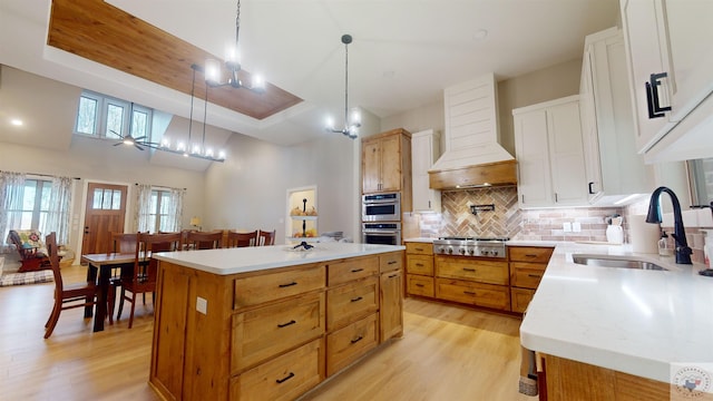 kitchen with custom exhaust hood, sink, backsplash, white cabinetry, and a kitchen island