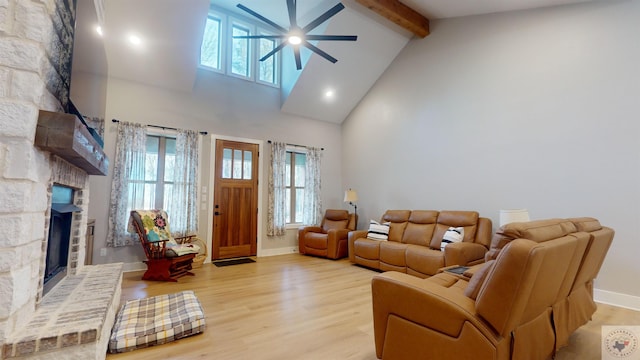 living room featuring ceiling fan, beamed ceiling, a stone fireplace, and light wood-type flooring