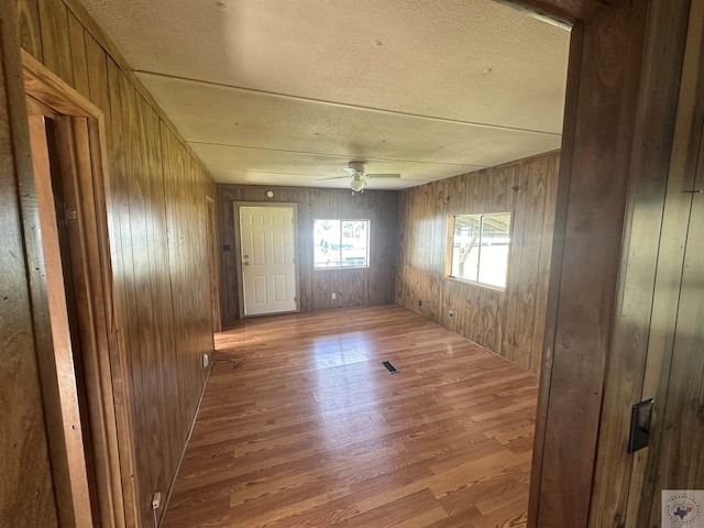 unfurnished room with ceiling fan, wood-type flooring, and wooden walls