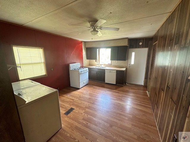 kitchen featuring white appliances, wood-type flooring, wooden walls, sink, and ceiling fan