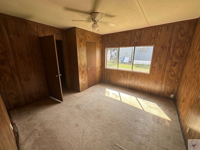 carpeted spare room featuring ceiling fan, wood walls, and a textured ceiling