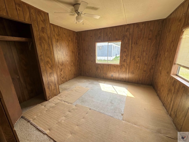 carpeted empty room with ceiling fan and wooden walls