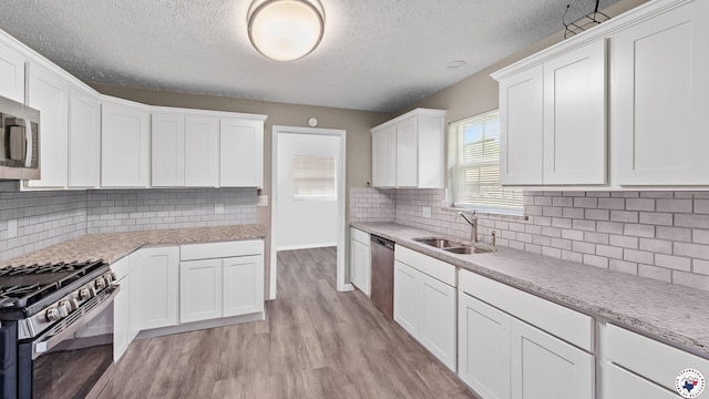 2401 E E Ave B, Hooks, TX 75561 - kitchen with stainless steel appliances, a sink, light wood-style flooring, a textured ceiling, and white cabinetry