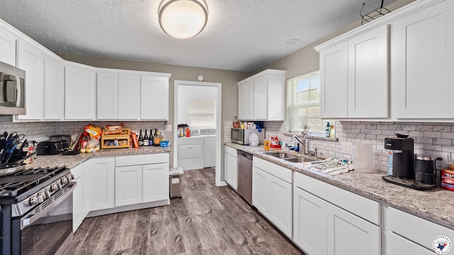 kitchen featuring wood finished floors, a textured ceiling, a sink, washer and dryer, and appliances with stainless steel finishes