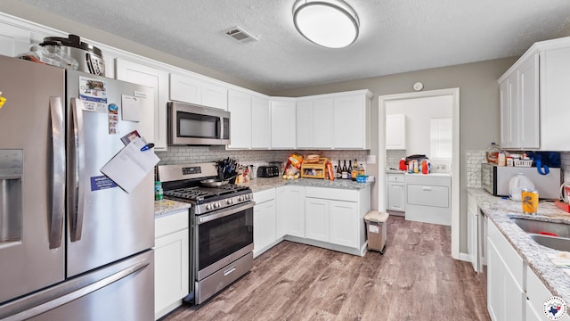 kitchen with backsplash, appliances with stainless steel finishes, white cabinetry, and light wood-style flooring