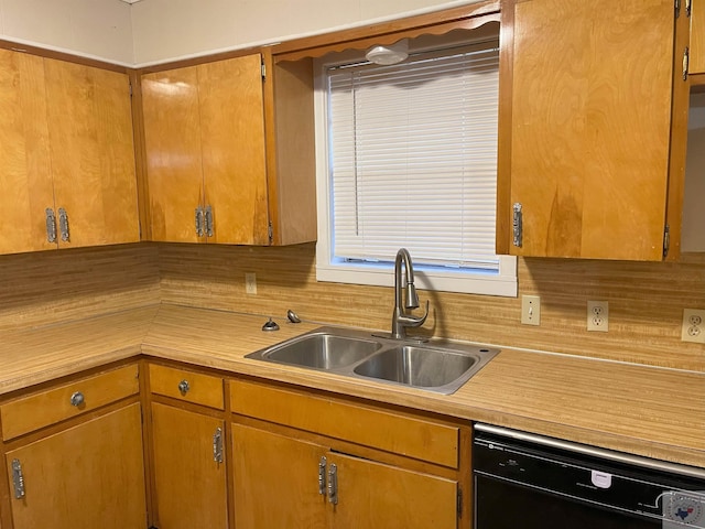 kitchen featuring brown cabinetry, black dishwasher, light countertops, and a sink