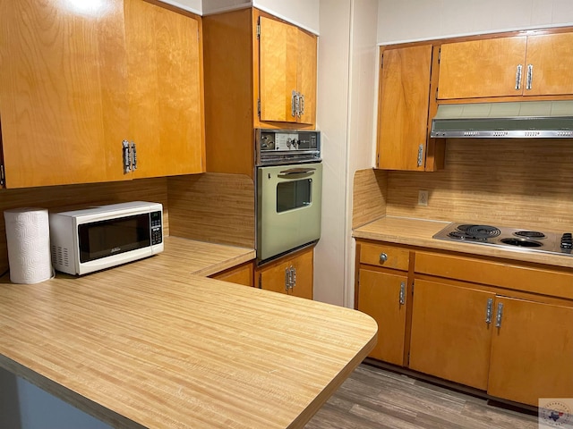 kitchen featuring light countertops, white microwave, wall oven, stainless steel electric cooktop, and under cabinet range hood