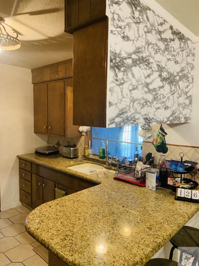 kitchen featuring sink, kitchen peninsula, light stone countertops, and a textured ceiling