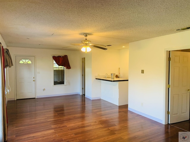 unfurnished living room featuring ceiling fan, dark wood-type flooring, and a textured ceiling