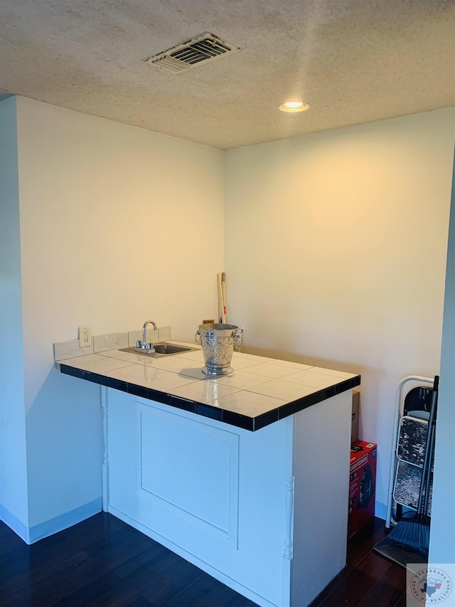 kitchen with sink, a textured ceiling, kitchen peninsula, and tile counters