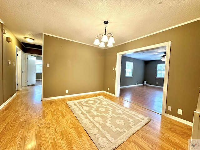 empty room featuring light wood-type flooring, an inviting chandelier, ornamental molding, and a textured ceiling