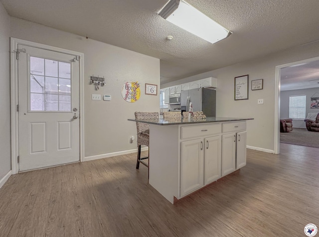 15 Annadale Dr, Maud, TX 75567 - kitchen featuring appliances with stainless steel finishes, white cabinetry, wood finished floors, a center island, and a textured ceiling
