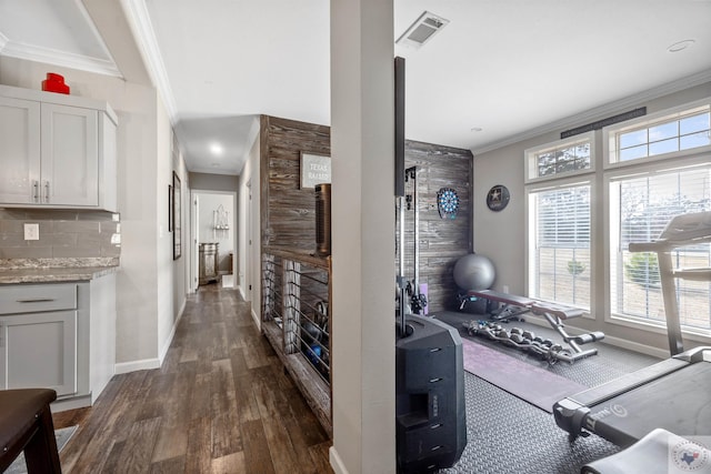 exercise room featuring ornamental molding, dark wood-style flooring, visible vents, and baseboards