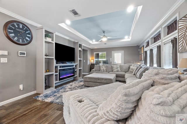 living room with a tray ceiling, dark wood-style flooring, visible vents, ornamental molding, and baseboards