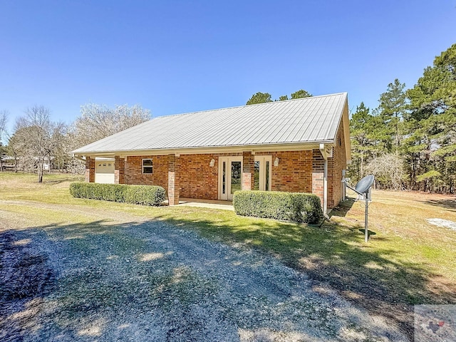 view of front facade with metal roof, a front yard, brick siding, and an attached garage