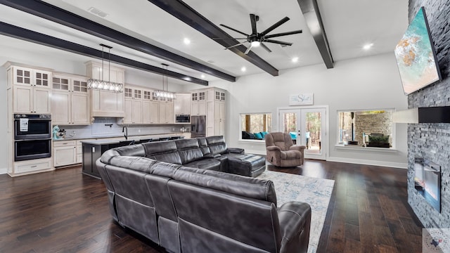 living area featuring beam ceiling, french doors, dark wood-type flooring, a stone fireplace, and baseboards