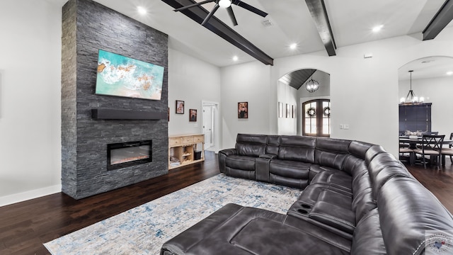 living area featuring arched walkways, a stone fireplace, and wood finished floors