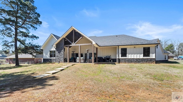 rear view of property with stone siding, a shingled roof, and a lawn