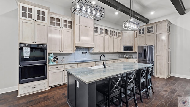 kitchen featuring light stone counters, tasteful backsplash, a kitchen island with sink, beamed ceiling, and black appliances