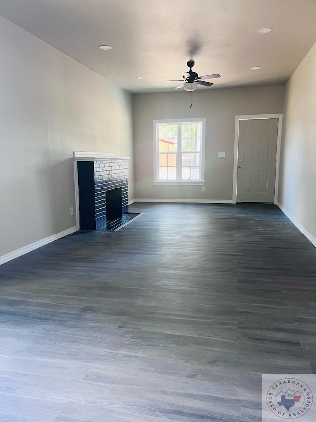 unfurnished living room featuring ceiling fan, dark wood-type flooring, and a brick fireplace