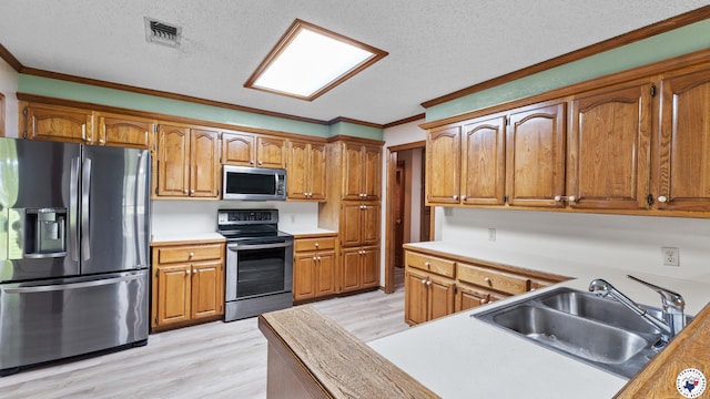 1135 Cook Rd, Texarkana, AR 71854 - kitchen featuring stainless steel appliances, light wood finished floors, crown molding, brown cabinets, and a textured ceiling